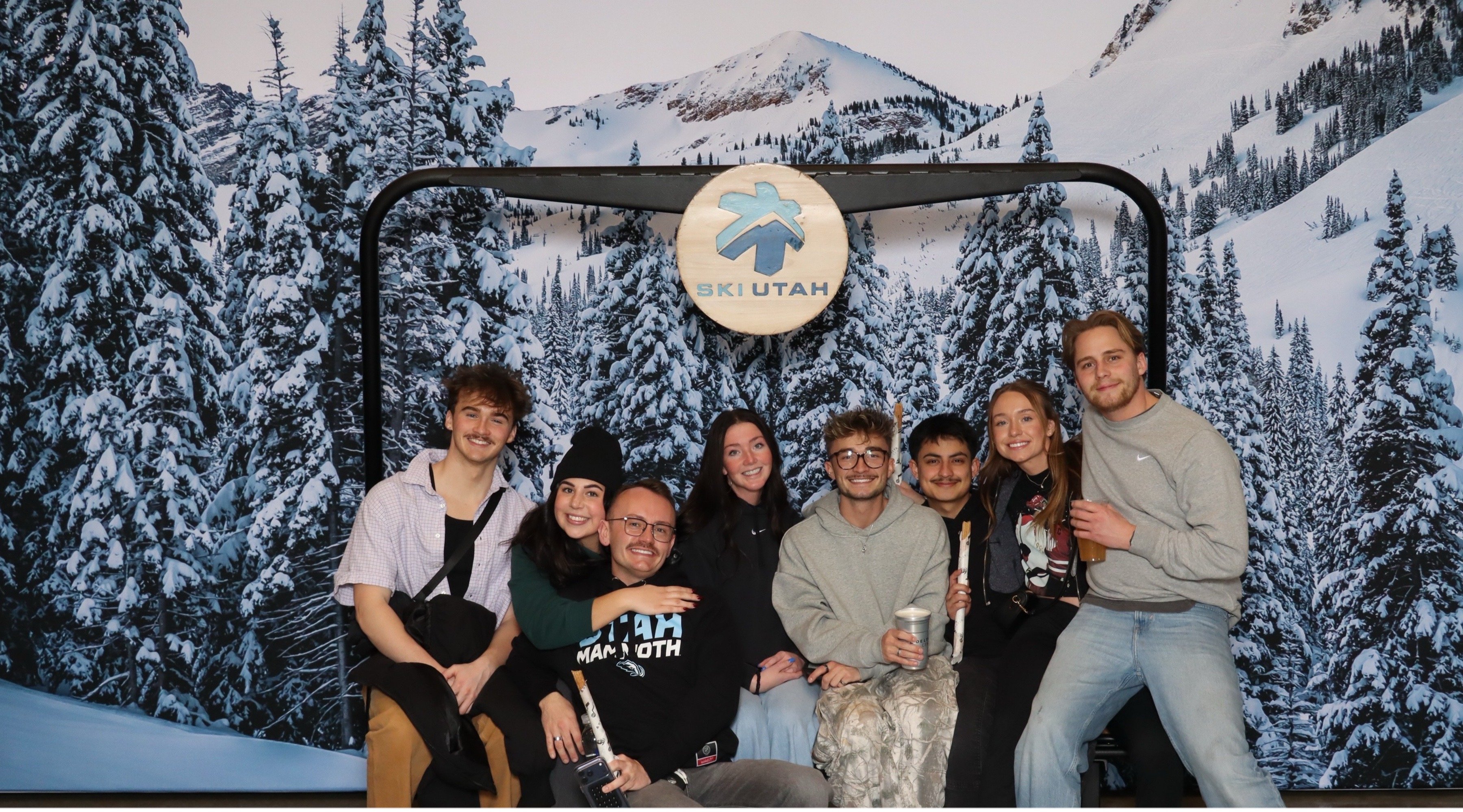 A group of guests posing before a snowy mountain backdrop under a round Ski Utah sign
