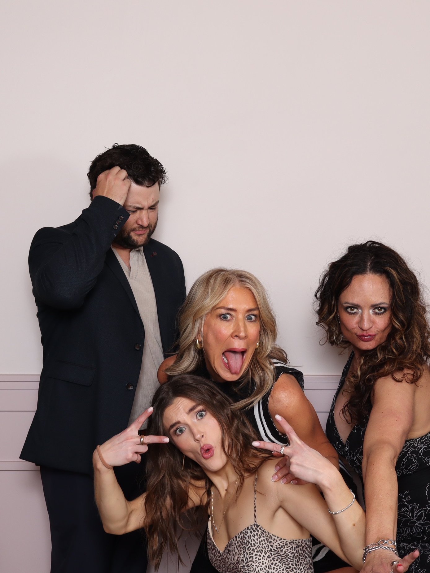 Four guests pull silly faces against a plain light backdrop, one sticking out her tongue