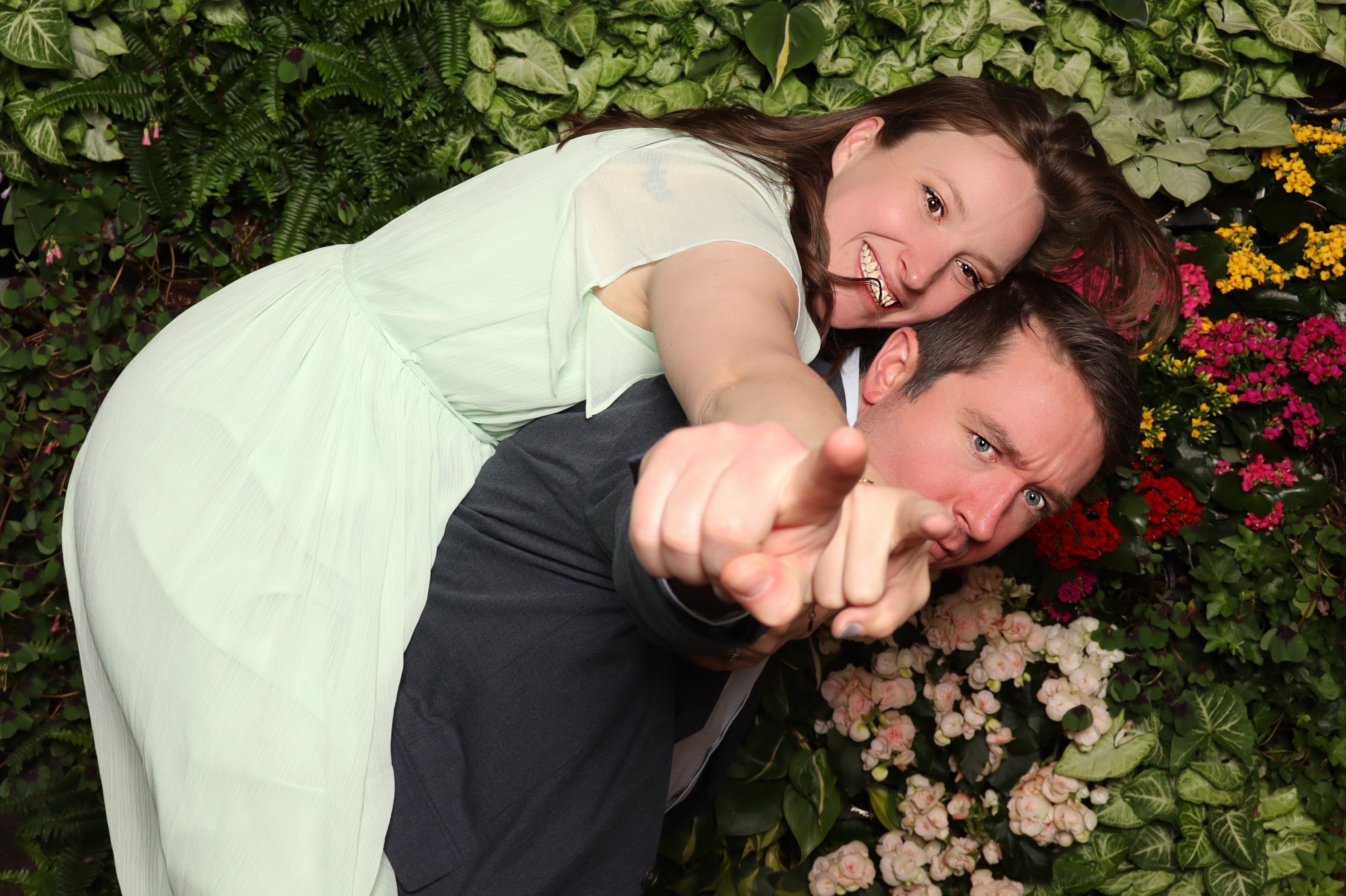 A couple laughing together at the booth in front of the greenery wall