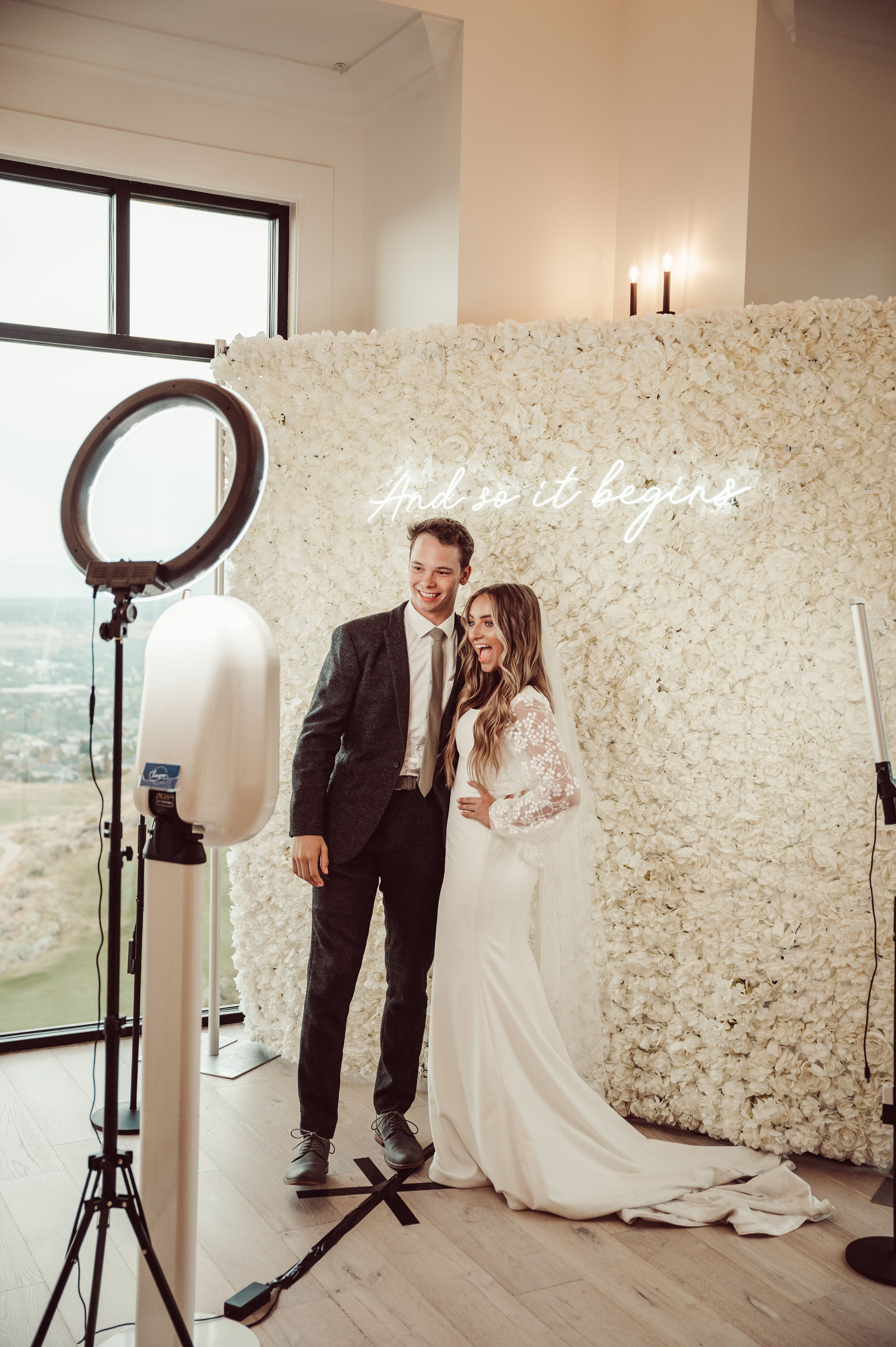 A bride and groom standing beside the booth at a white floral wall