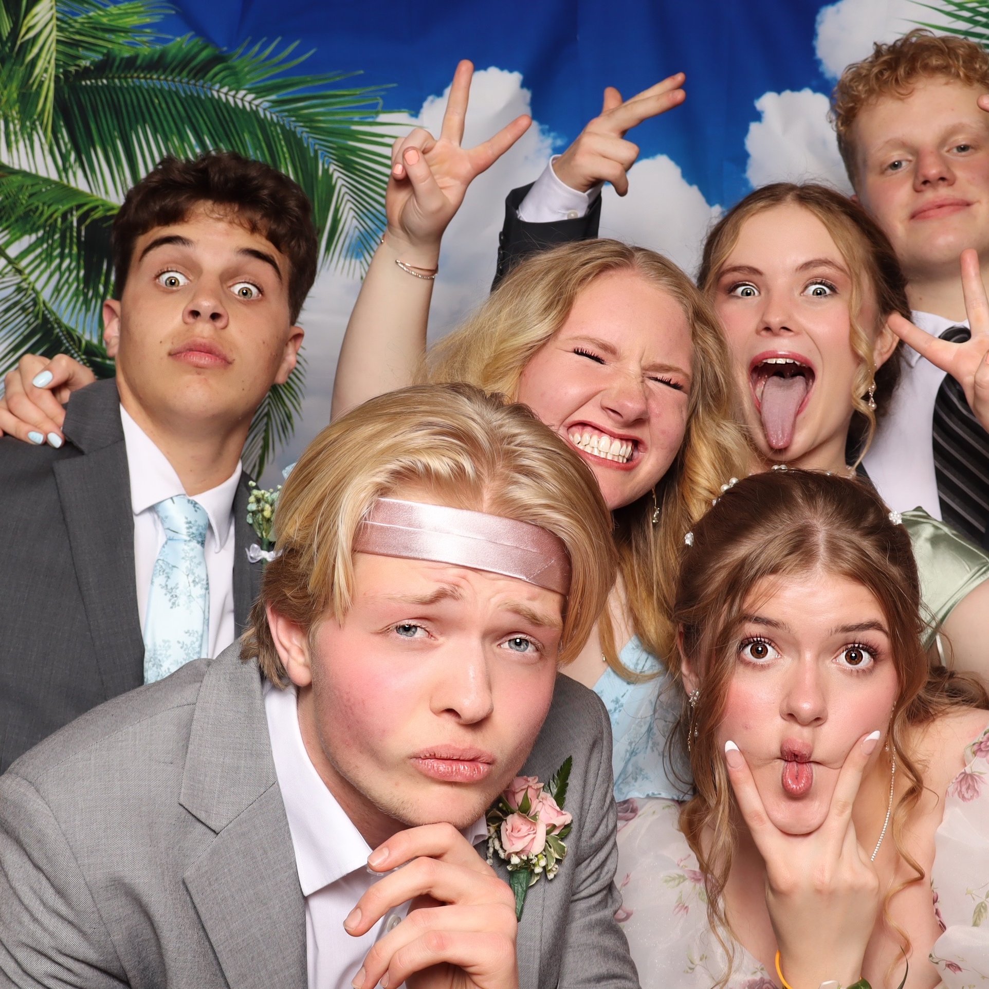 Six students in formalwear crowding into one frame at a sky backdrop