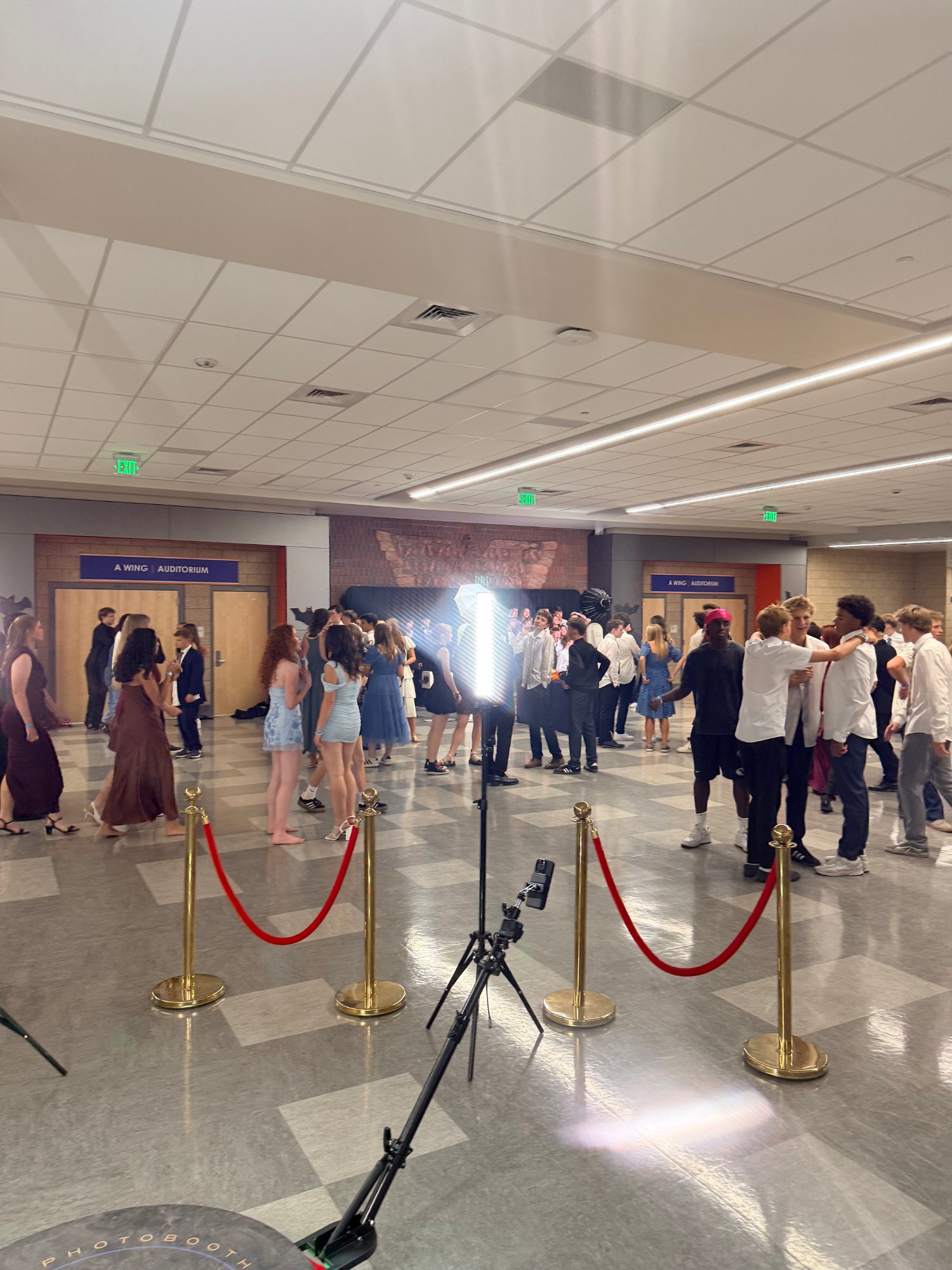 360 photo booth platform with gold stanchions and red ropes, a crowd of guests gathered in the hall behind